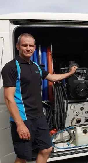 A man in a blue and black shirt is standing in front of a van.