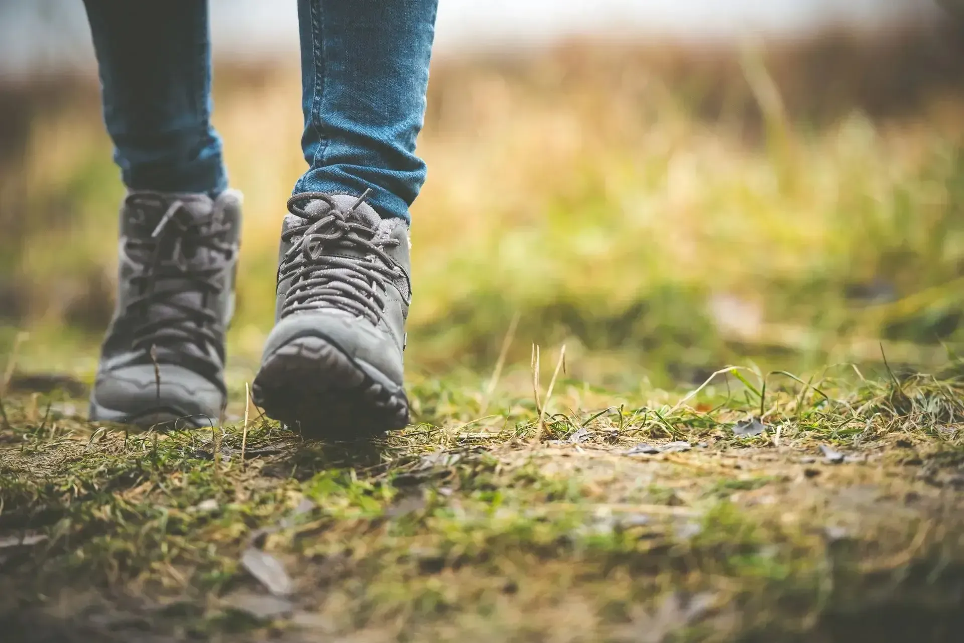 Person walking in hiking boots on a grassy path, close-up of feet and legs.