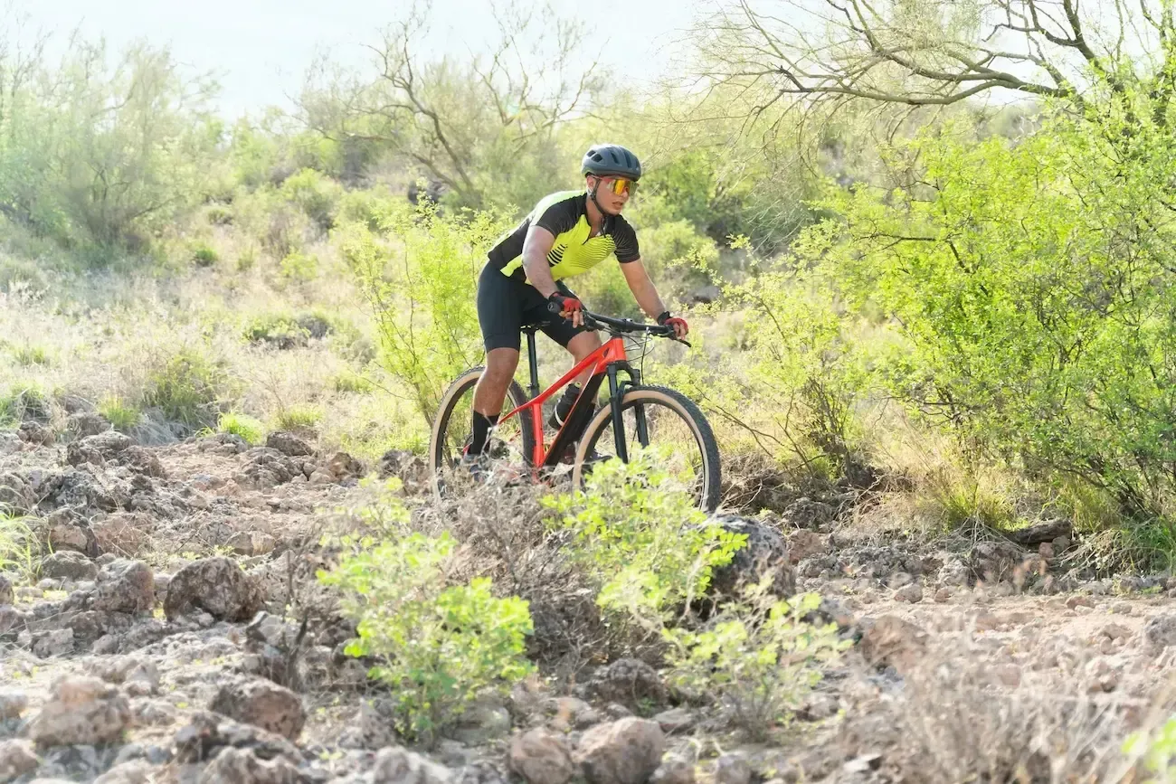 Mountain biker rides on a rocky trail with sparse vegetation.