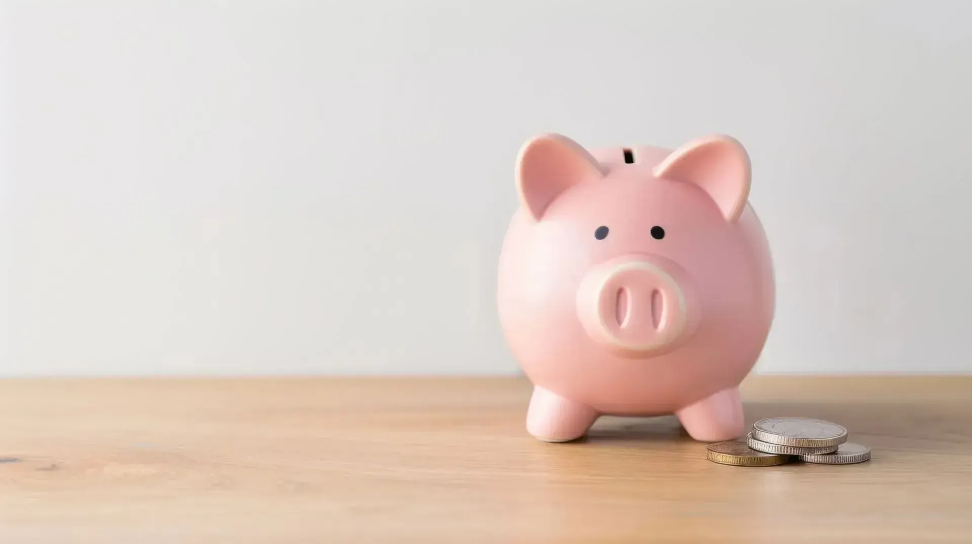 Pink piggy bank on a wooden surface with a few coins beside it.
