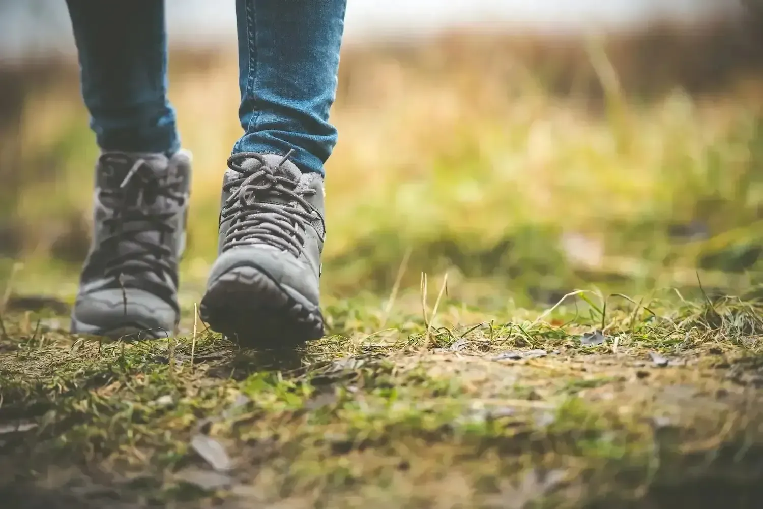 Person walking in hiking boots on a grassy path, close-up of feet and legs.