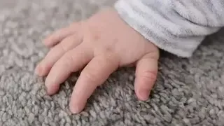 Close-up of a baby's hand on a gray carpet, wearing a gray and white striped sleeve.