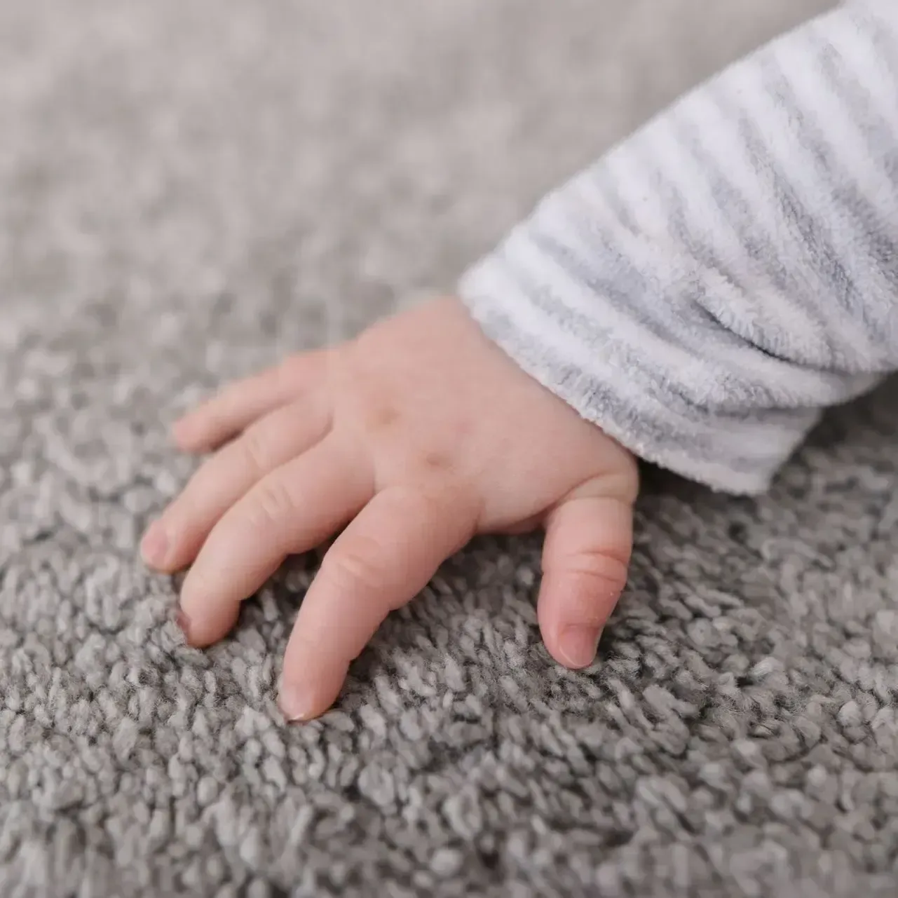 A baby 's hand is crawling on a gray carpet