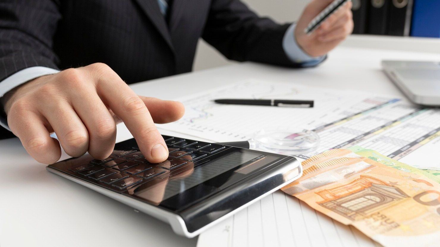 Un hombre de traje usa una calculadora mientras sostiene un bolígrafo.