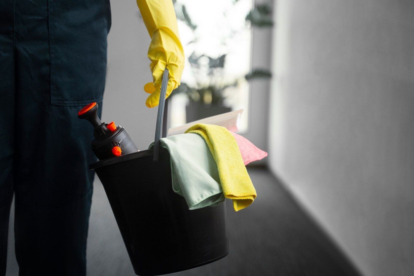 Una persona que lleva guantes amarillos sostiene un balde con productos de limpieza.