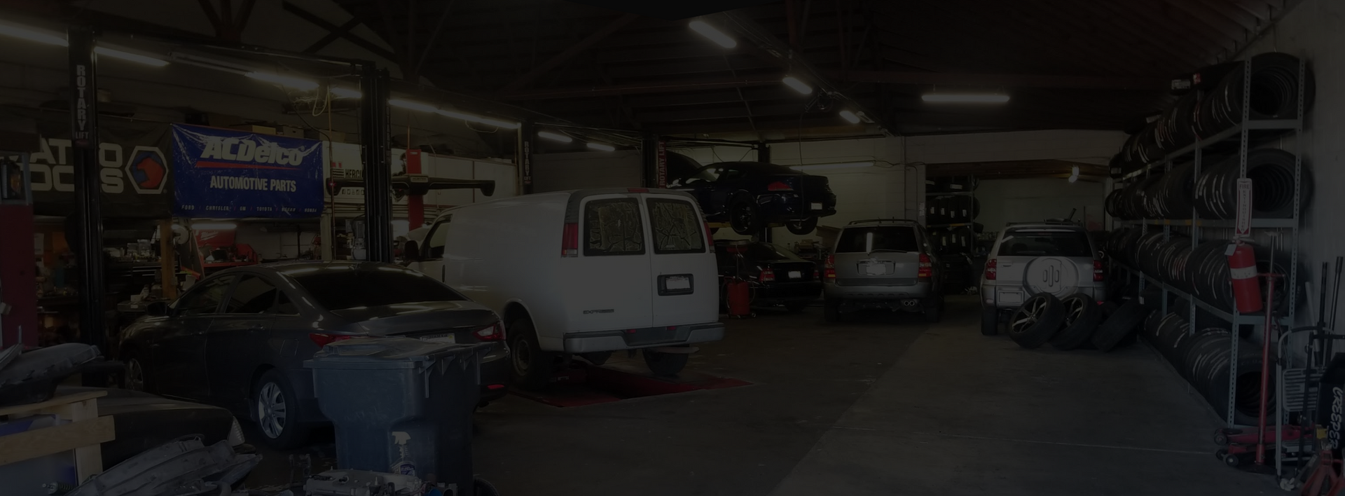 Interior of an auto repair shop with vehicles, tools, and equipment. A banner hangs in the background. | Good Guys Auto Care & Tires