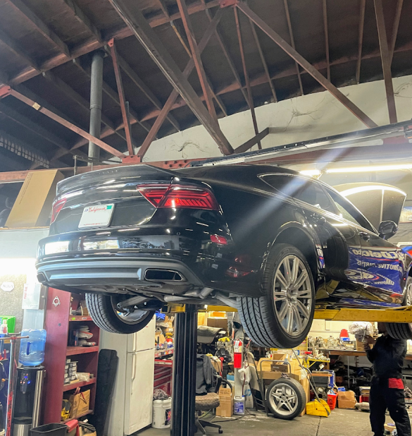 Black car on a lift inside a garage. A mechanic works beneath the car. | Good Guys Auto Care & Tire