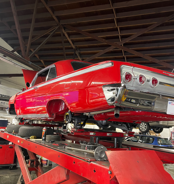 Red classic car on a red hydraulic lift inside a garage; car's undercarriage is exposed. | Good Guys Auto Care & Tires