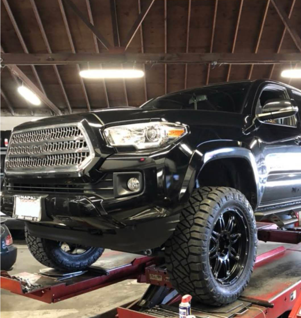 Black Toyota Tacoma truck raised on a red lift in a garage | Good Guys Auto Care & Tires