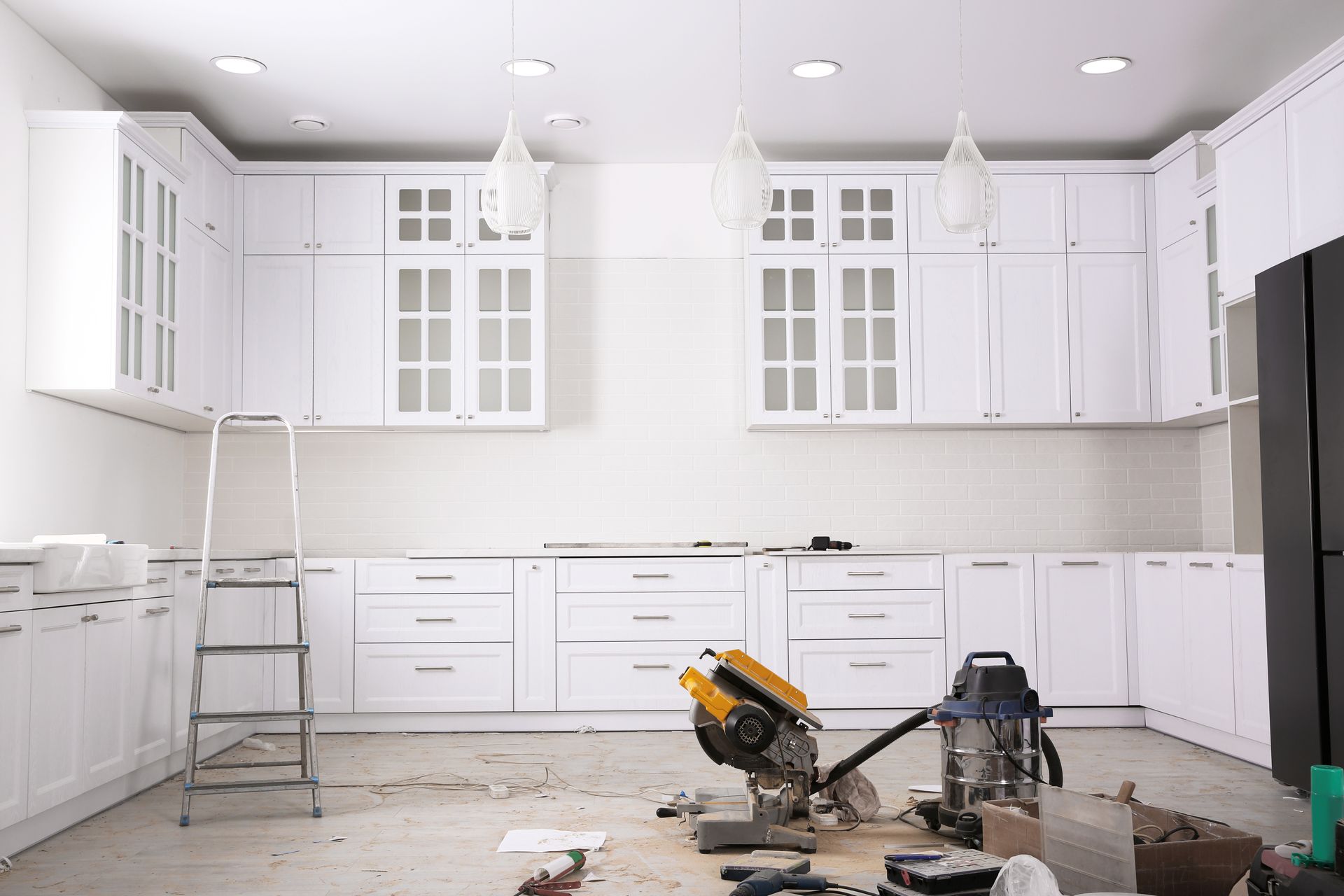 A completely white kitchen interior in the process of being renovated, with a saw on the floor.