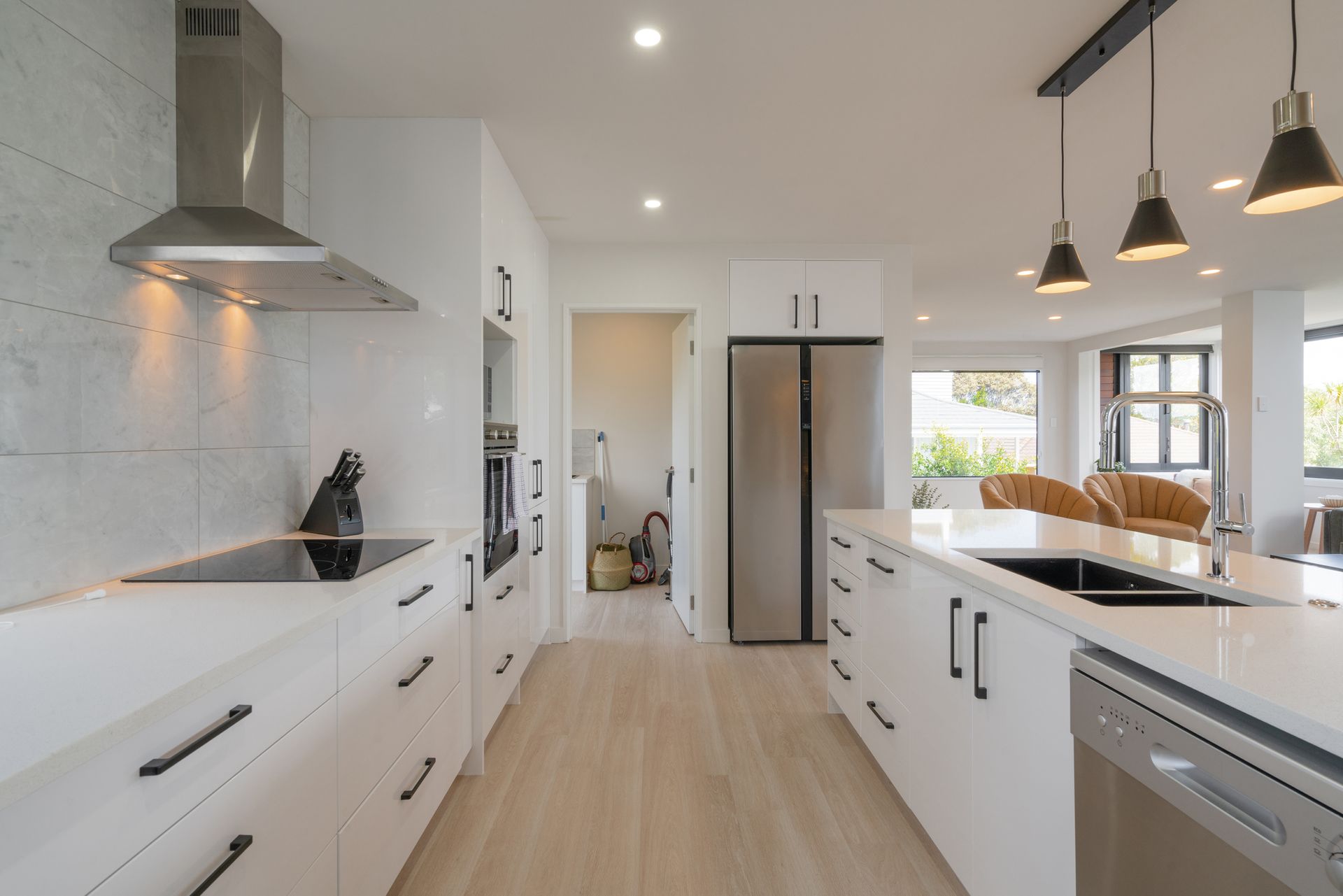 Modern white kitchen with stainless steel appliances, black accents, and light wood flooring.