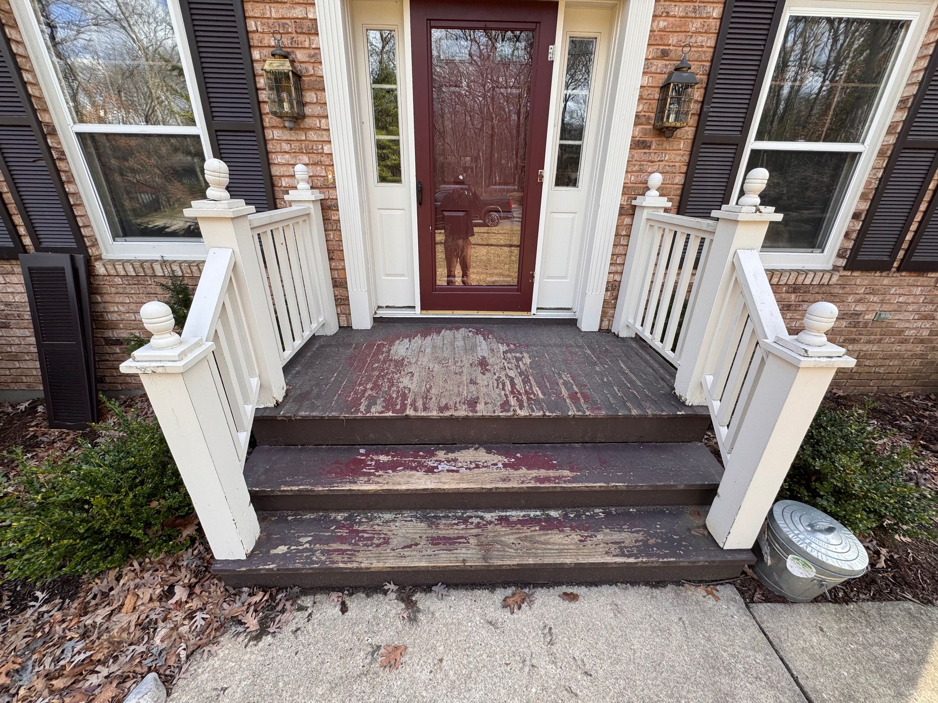 Wooden porch with peeling paint on steps and railings, brick home, front door.