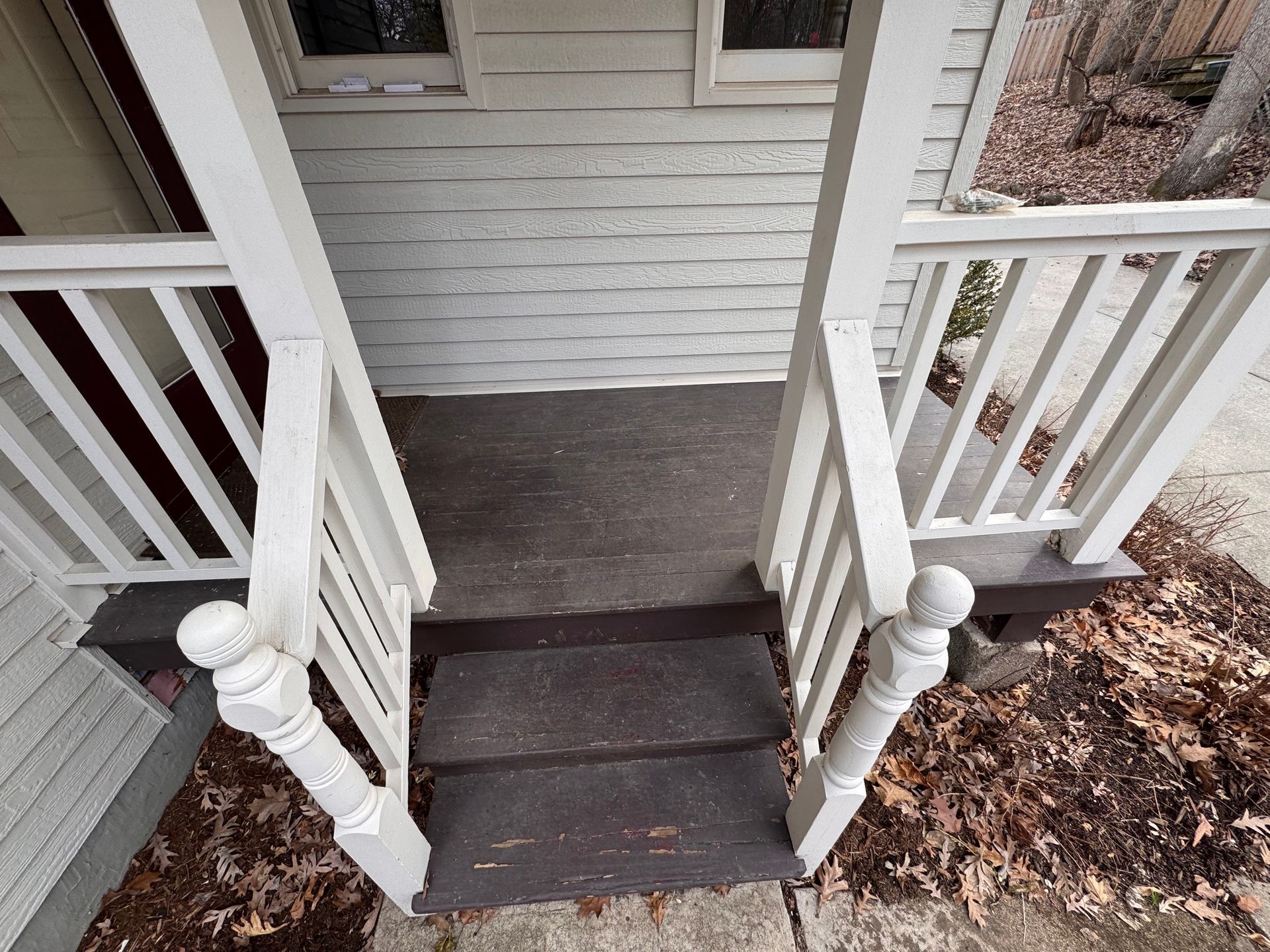 Exterior view of a porch with two steps, white railings, and a wooden door.