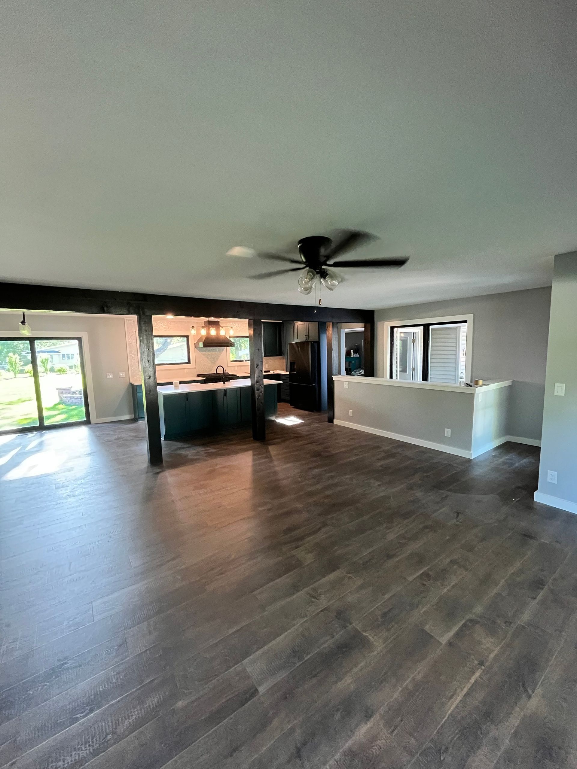 Open-concept living space with dark wood flooring, kitchen with teal cabinets, and a black ceiling fan.