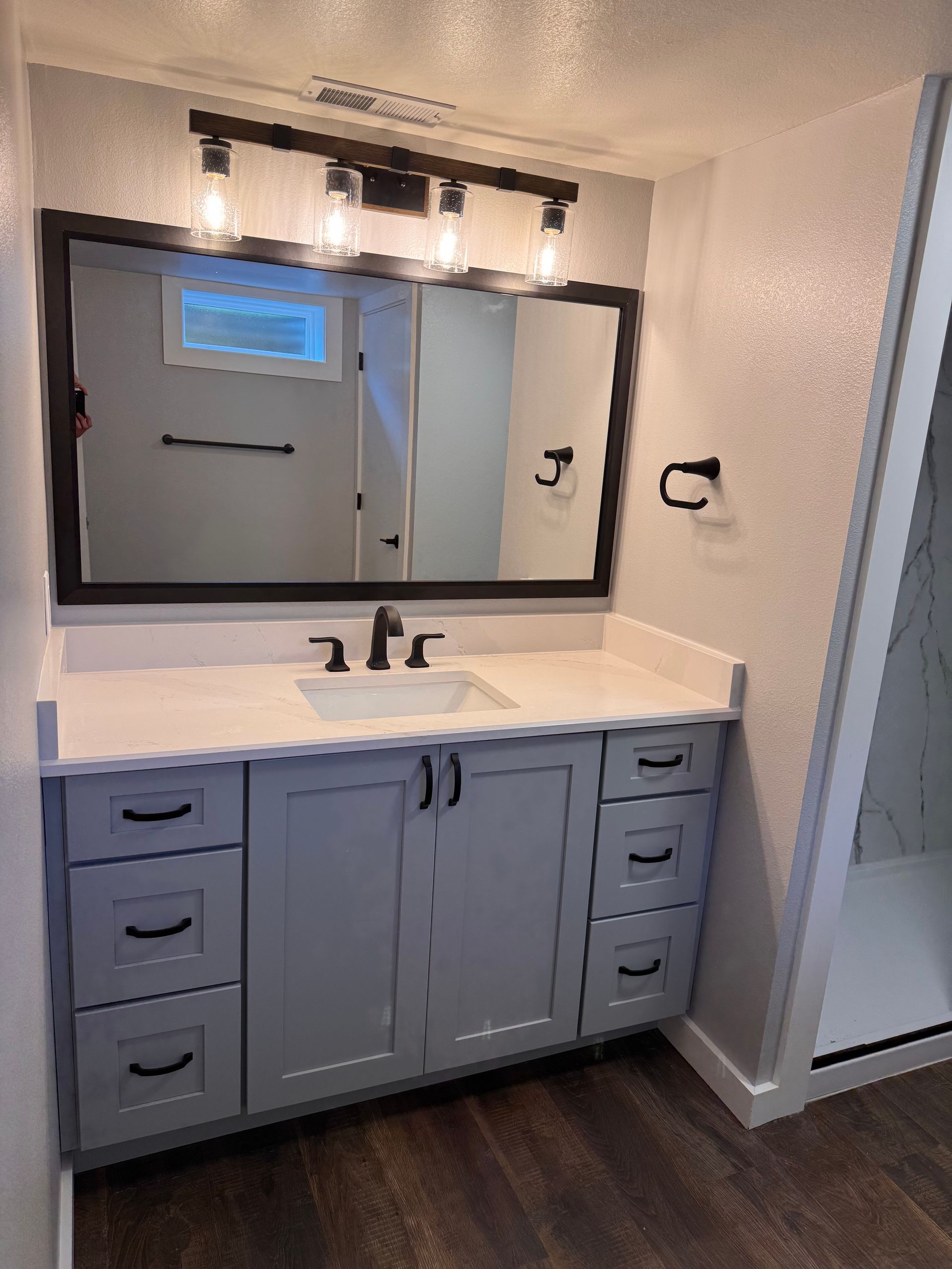 Bathroom vanity with gray cabinets, white countertop, dark mirror frame, and modern lighting.