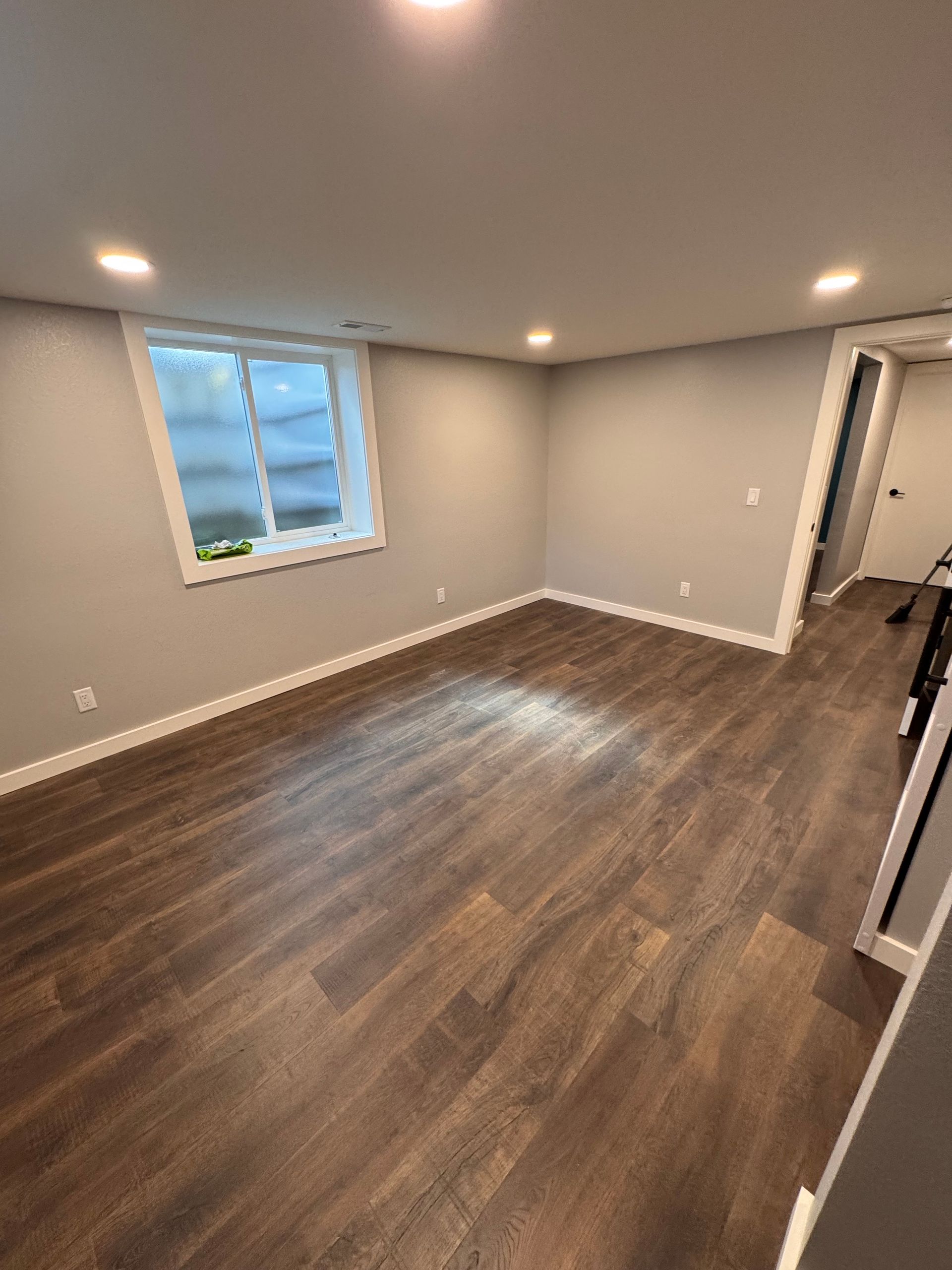 Empty room with wood-look flooring, gray walls, recessed lighting, and a small window.