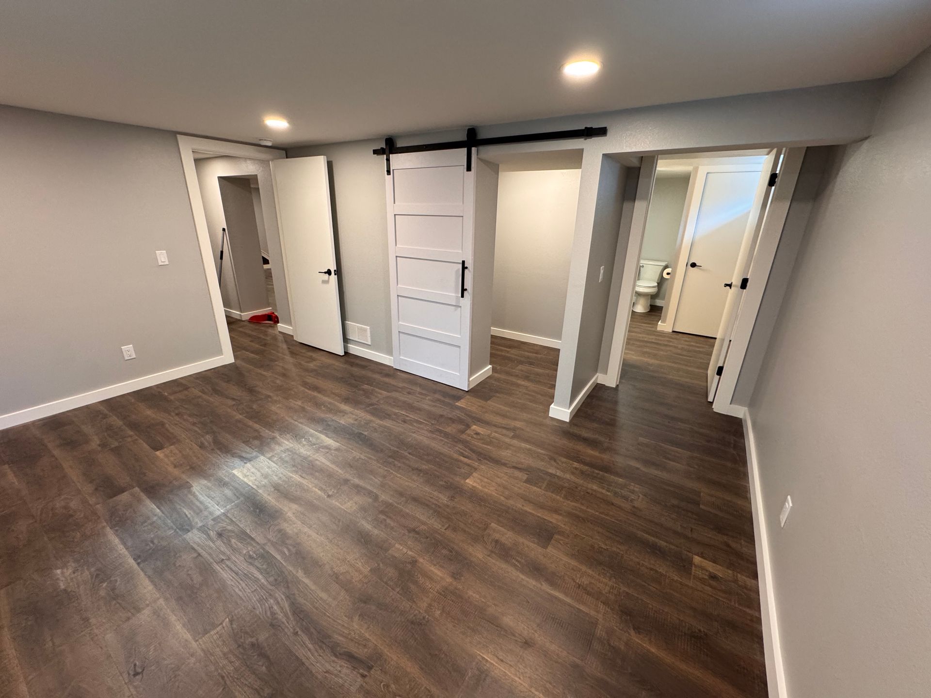 Bedroom with dark wood flooring, gray walls, recessed lighting, and white doors, including a sliding barn door.