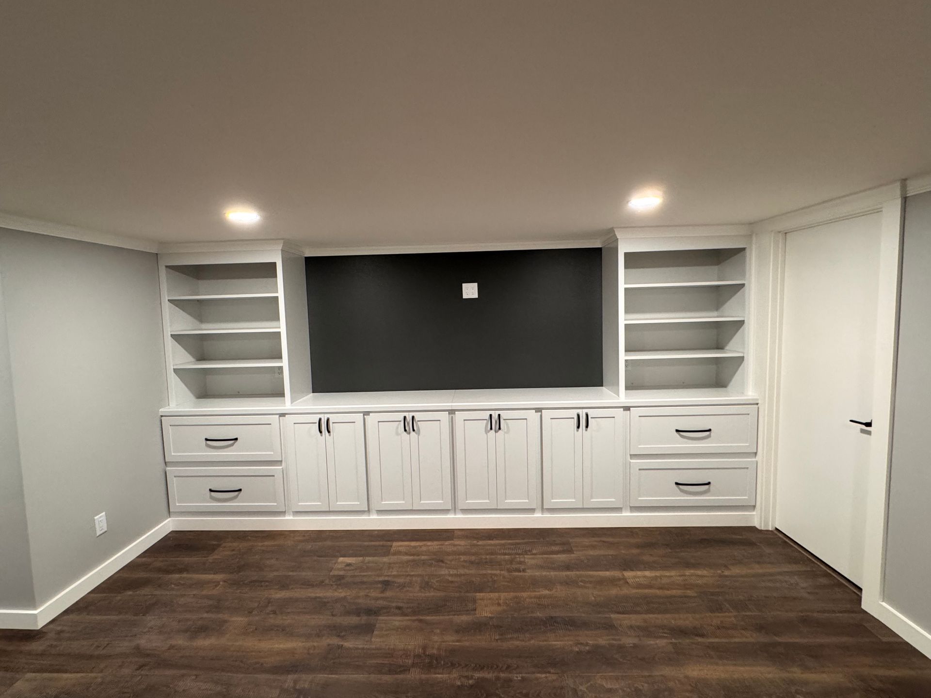 Built-in white entertainment center with shelves, drawers, and cabinet doors; dark accent wall for TV.