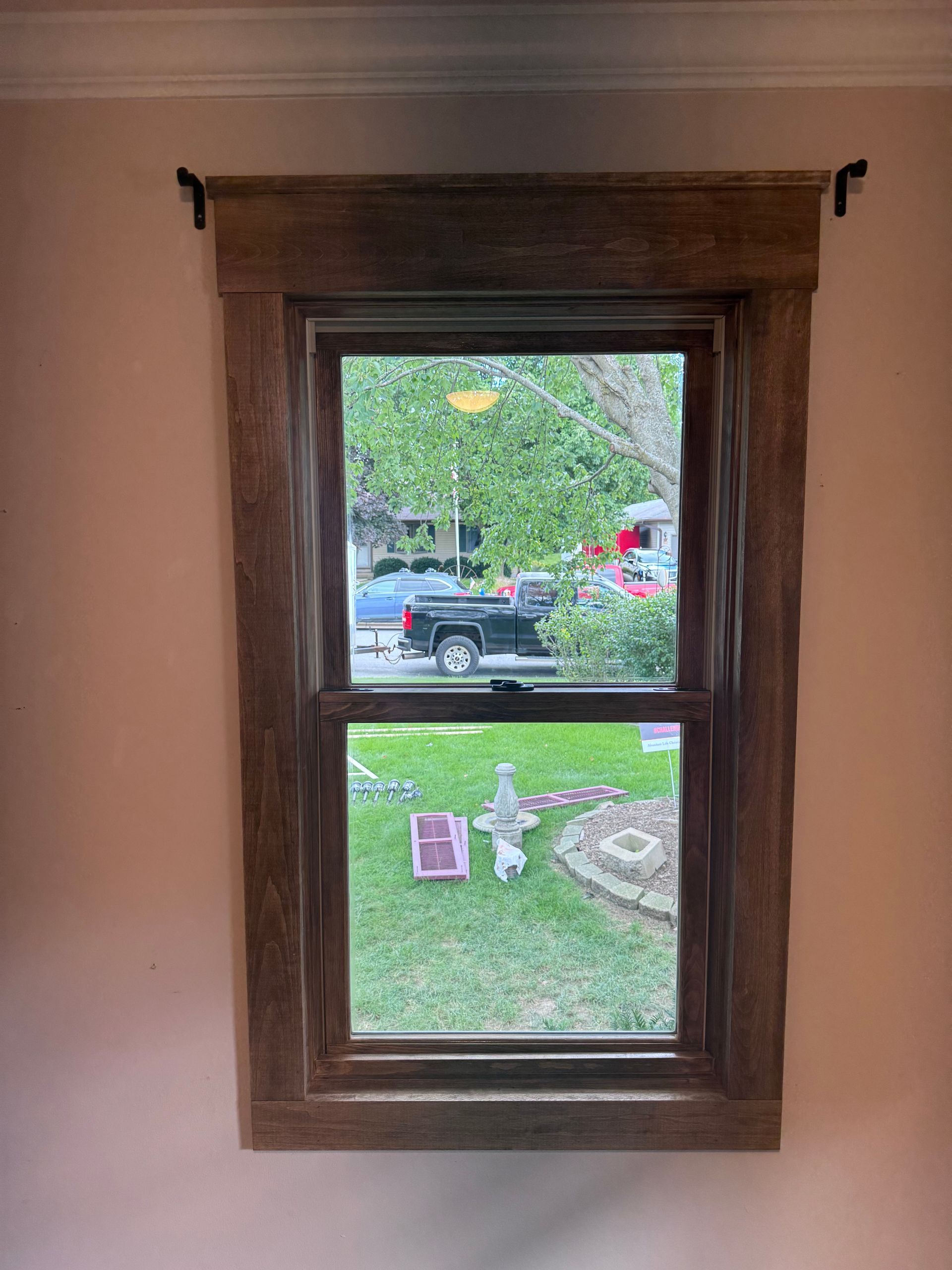 Window with rustic brown wooden trim; view of yard and street outside.