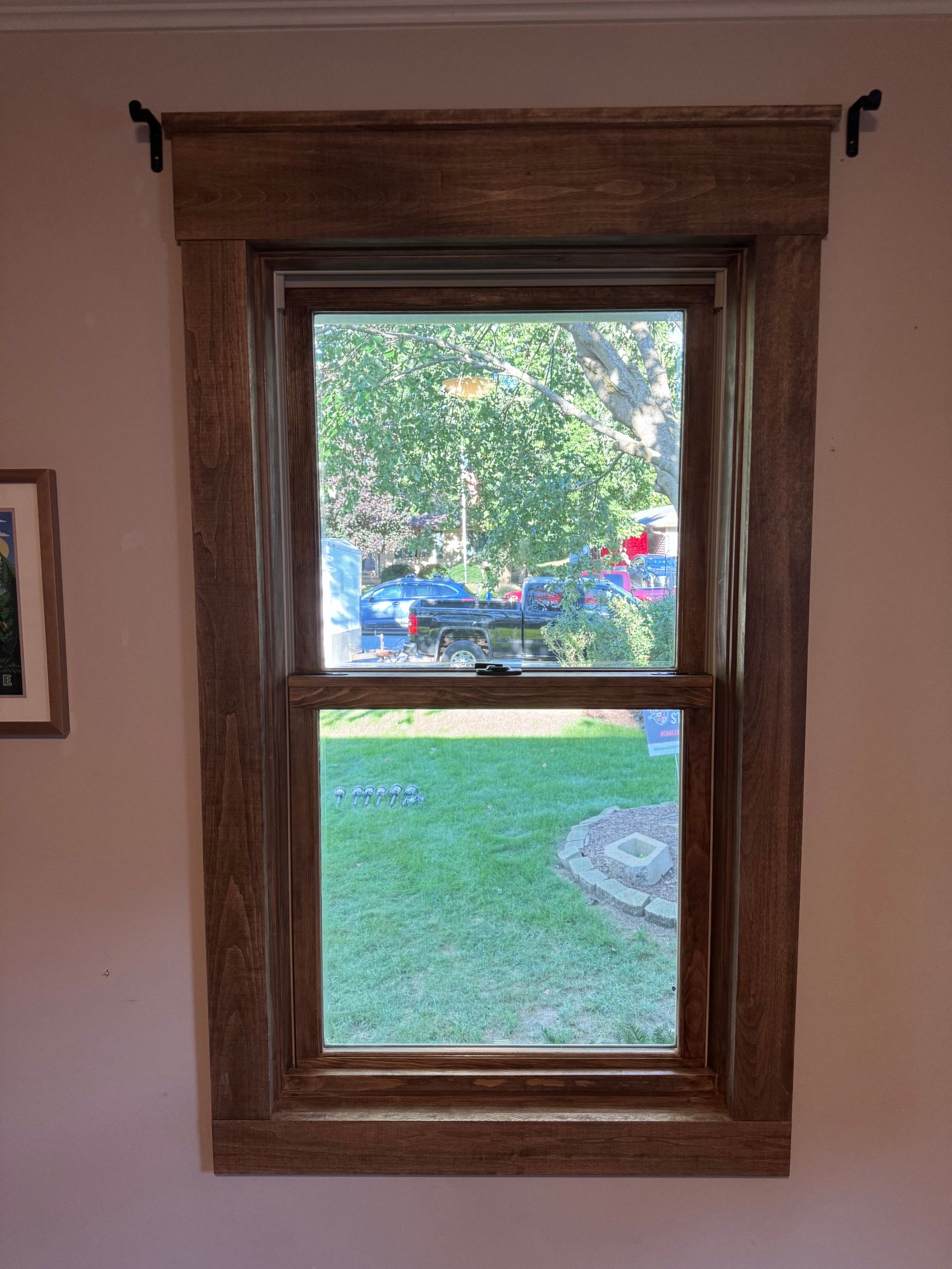 Wooden-framed window with view of yard; brown frame, curtain rods; pink wall.