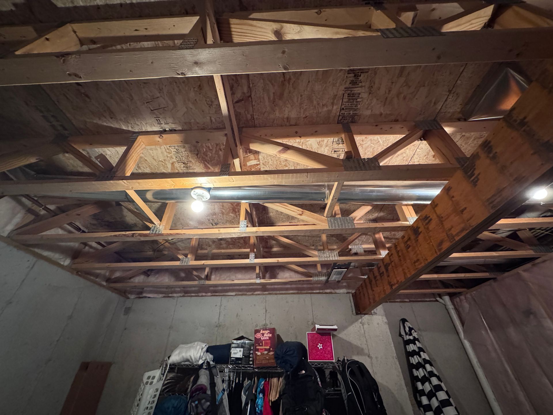 Basement ceiling with exposed wooden rafters and ductwork, with a rack of clothing below.