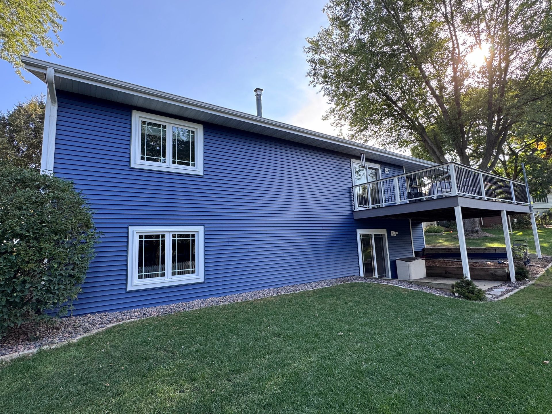 Blue house with white trim, windows, and deck, on a sunny day. Green lawn.