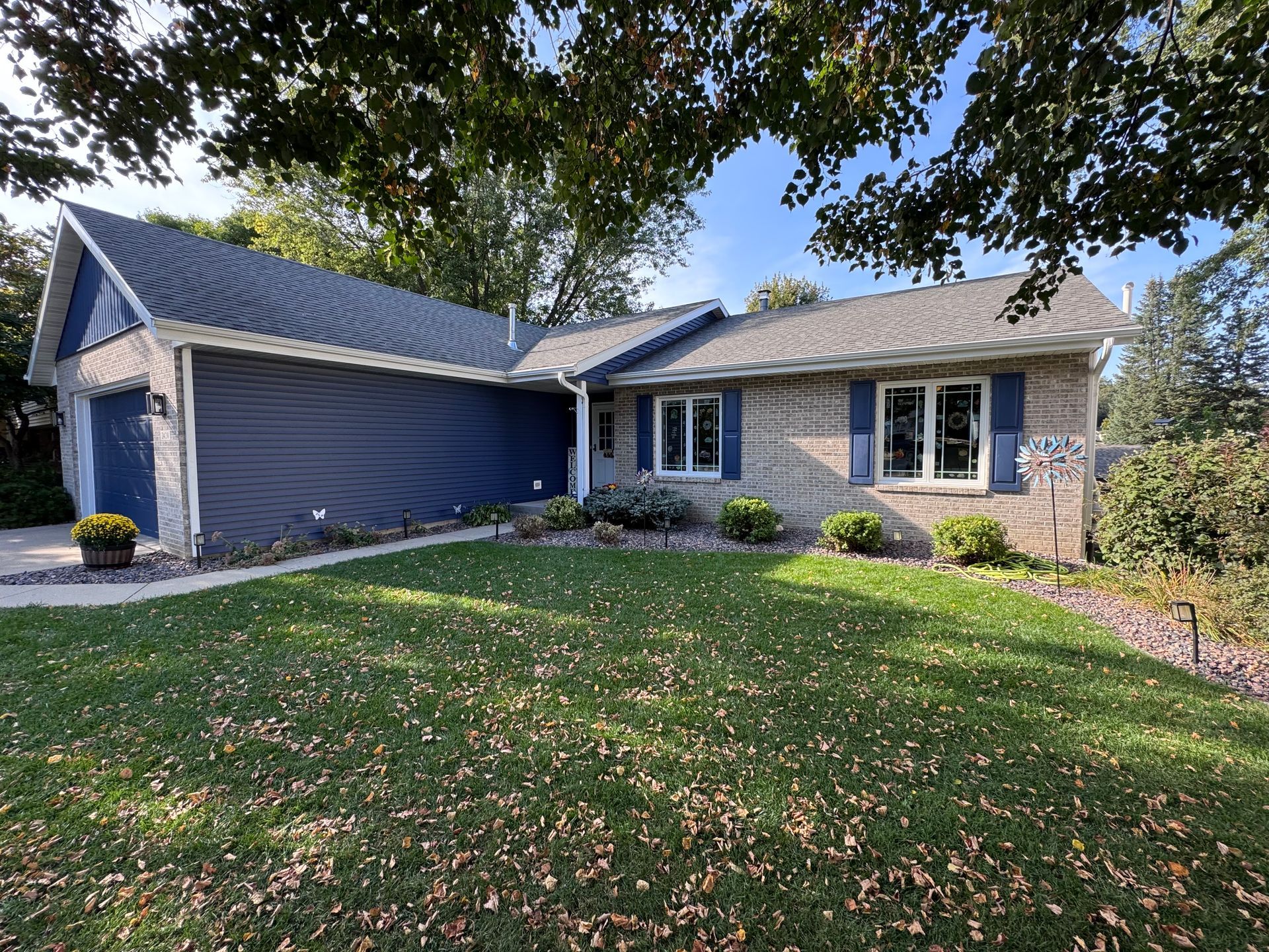 Blue-sided ranch-style house with gray roof, windows, and green lawn under a sunny sky.