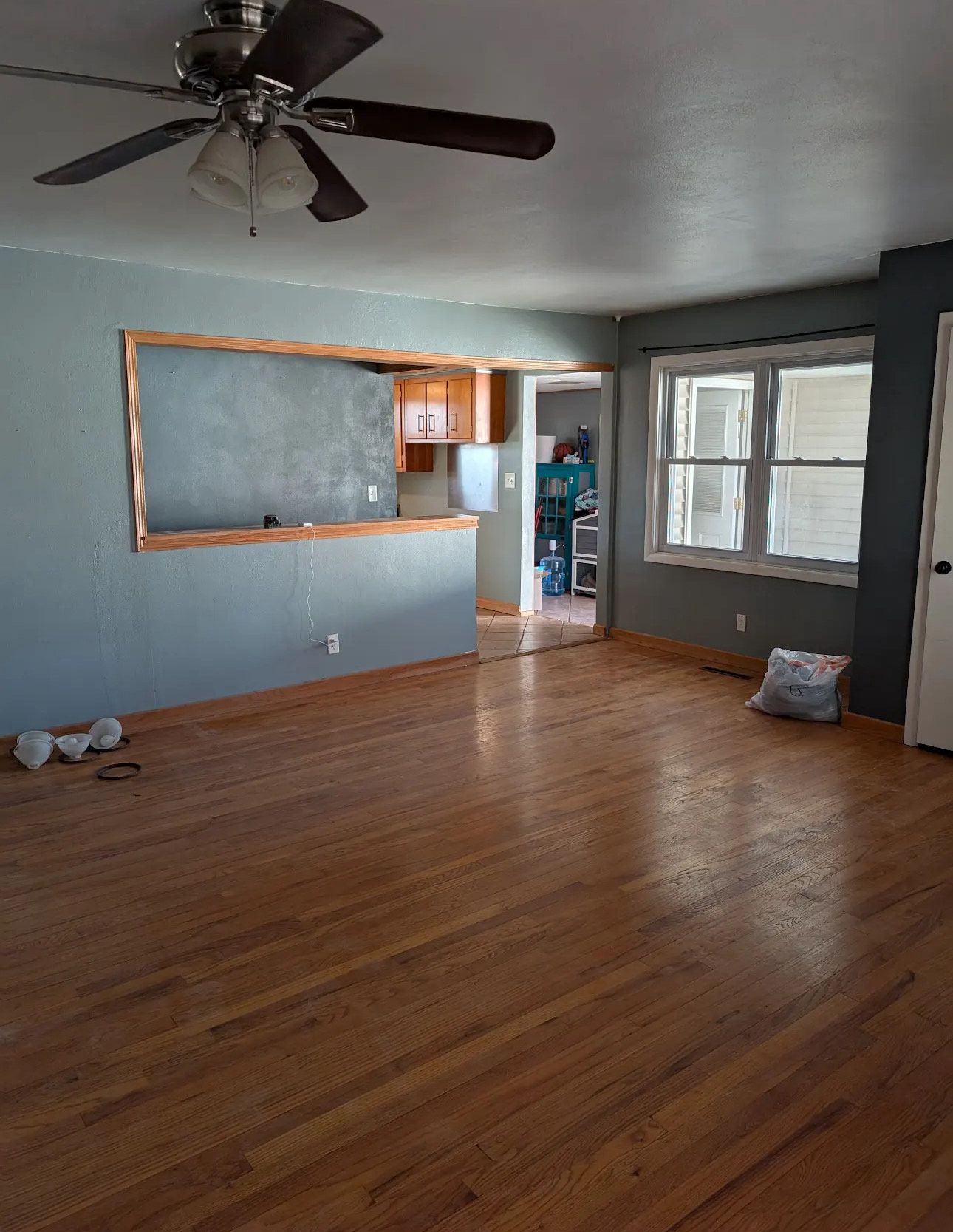Empty living room with wood floors, blue-gray walls, and a cutout to the kitchen.