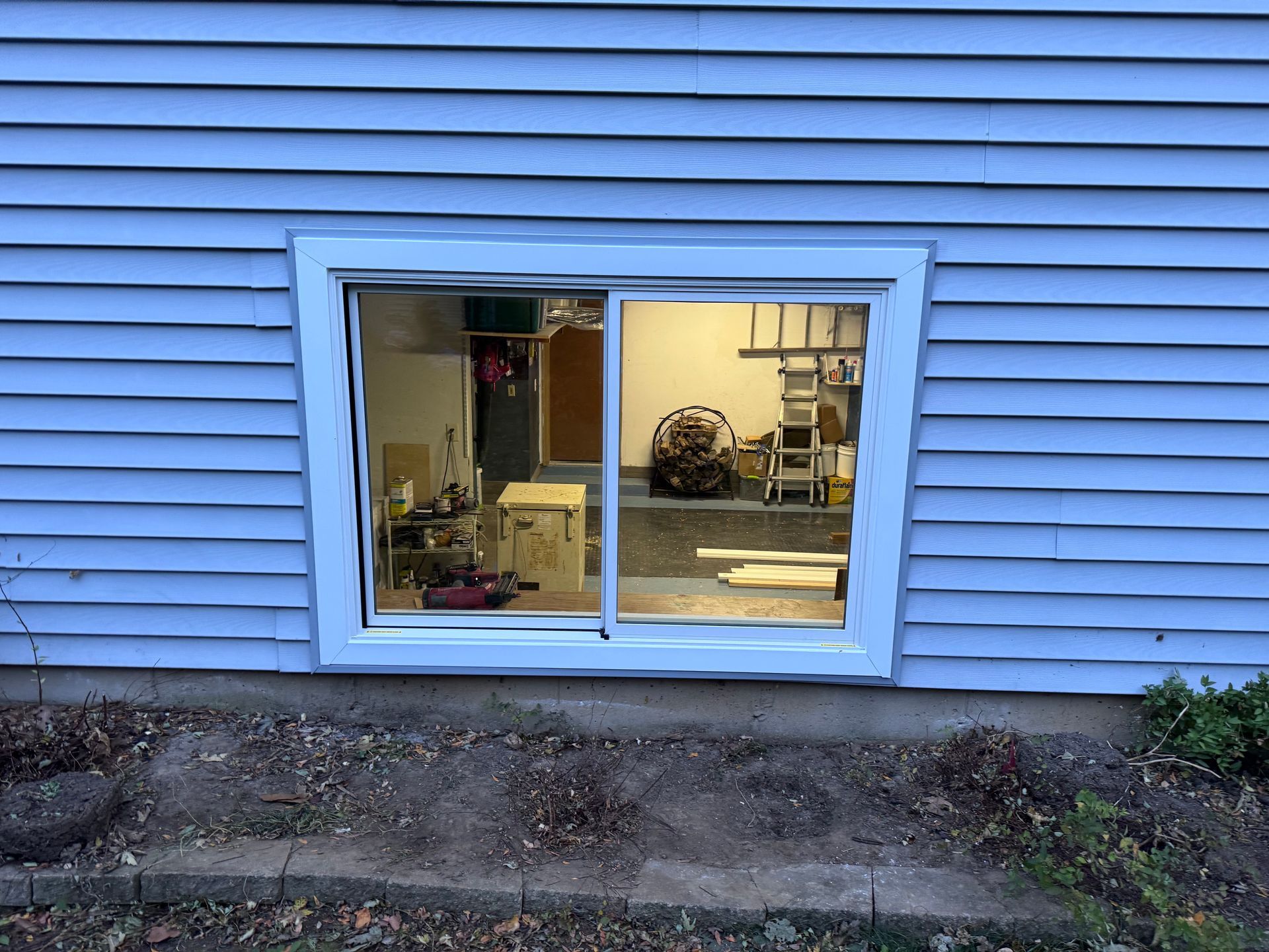 Window in a blue-sided building reflecting the inside of a garage with tools and a doorway.