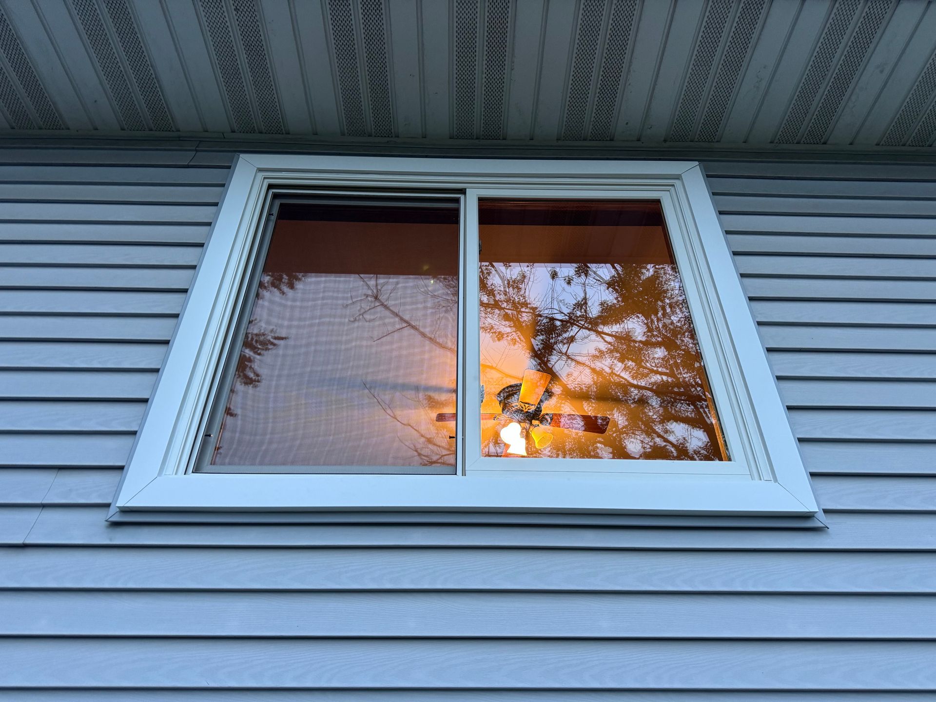 Window with a white frame on a blue-sided house reflects a sunset.