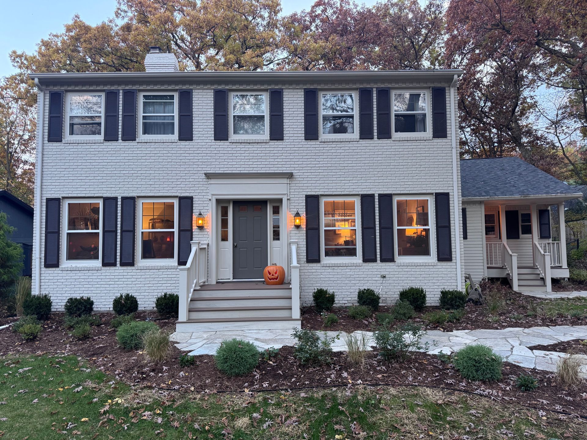Two-story brick house with black shutters, a gray door, and a pumpkin on the porch steps.