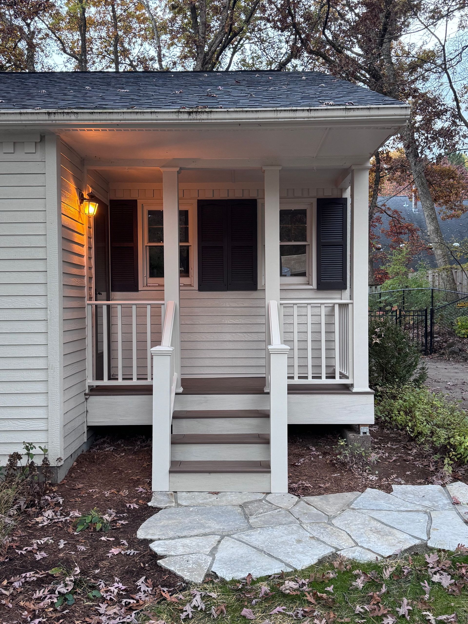 Small white porch with steps, brown door, black shutters, and stone path.