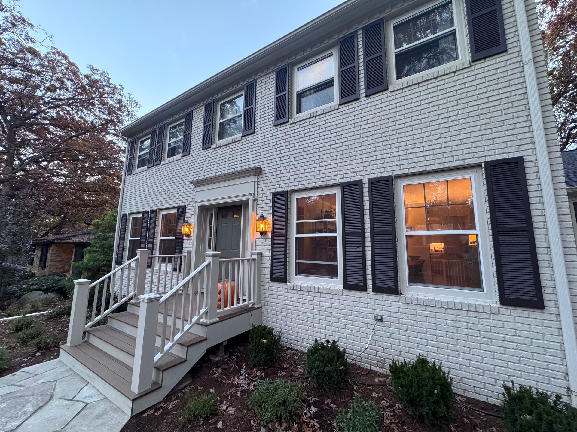 Two-story brick house with black shutters, steps, and front porch.