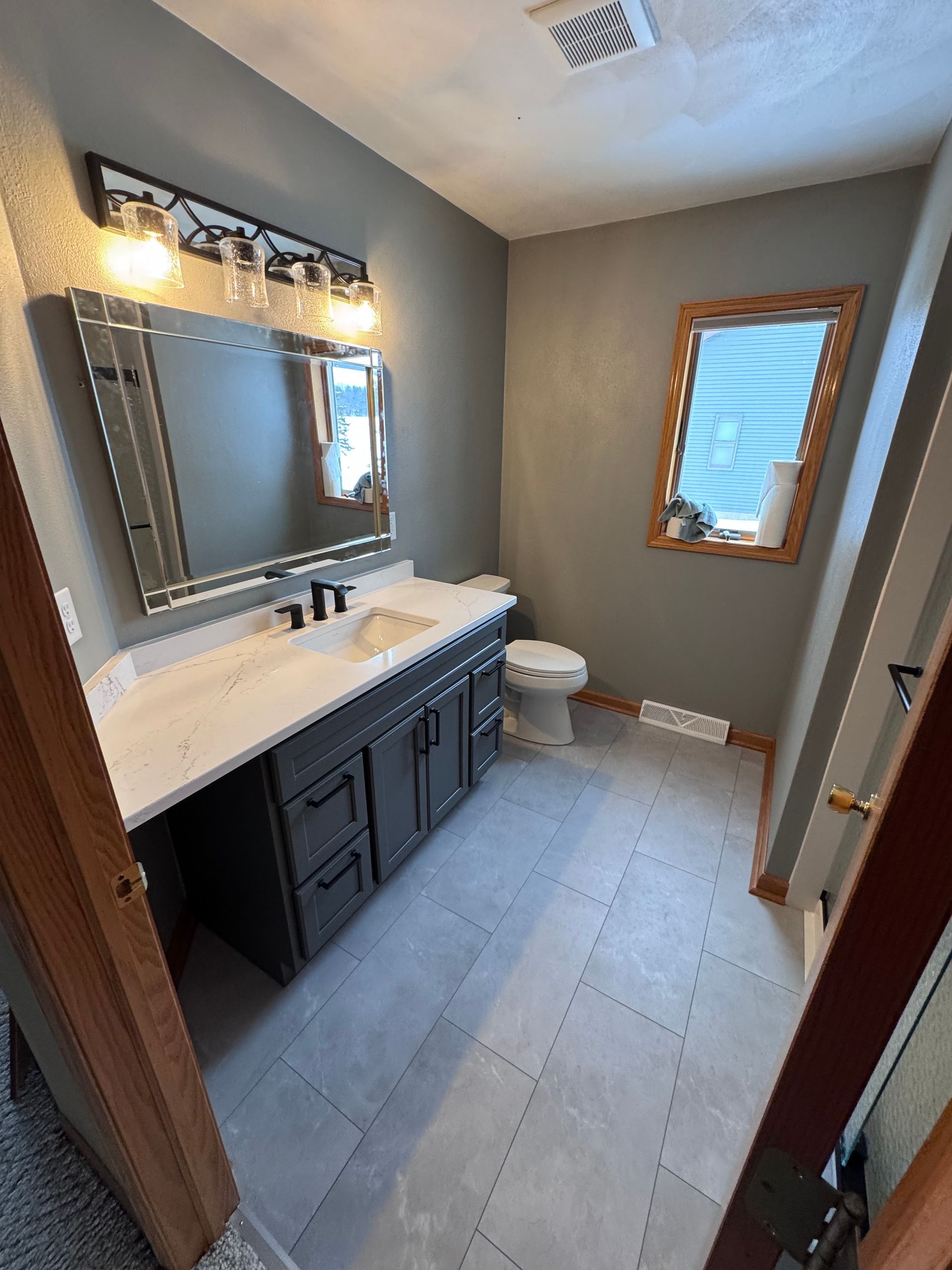 Bathroom with gray walls, vanity, mirror, toilet, and gray tiled floor.