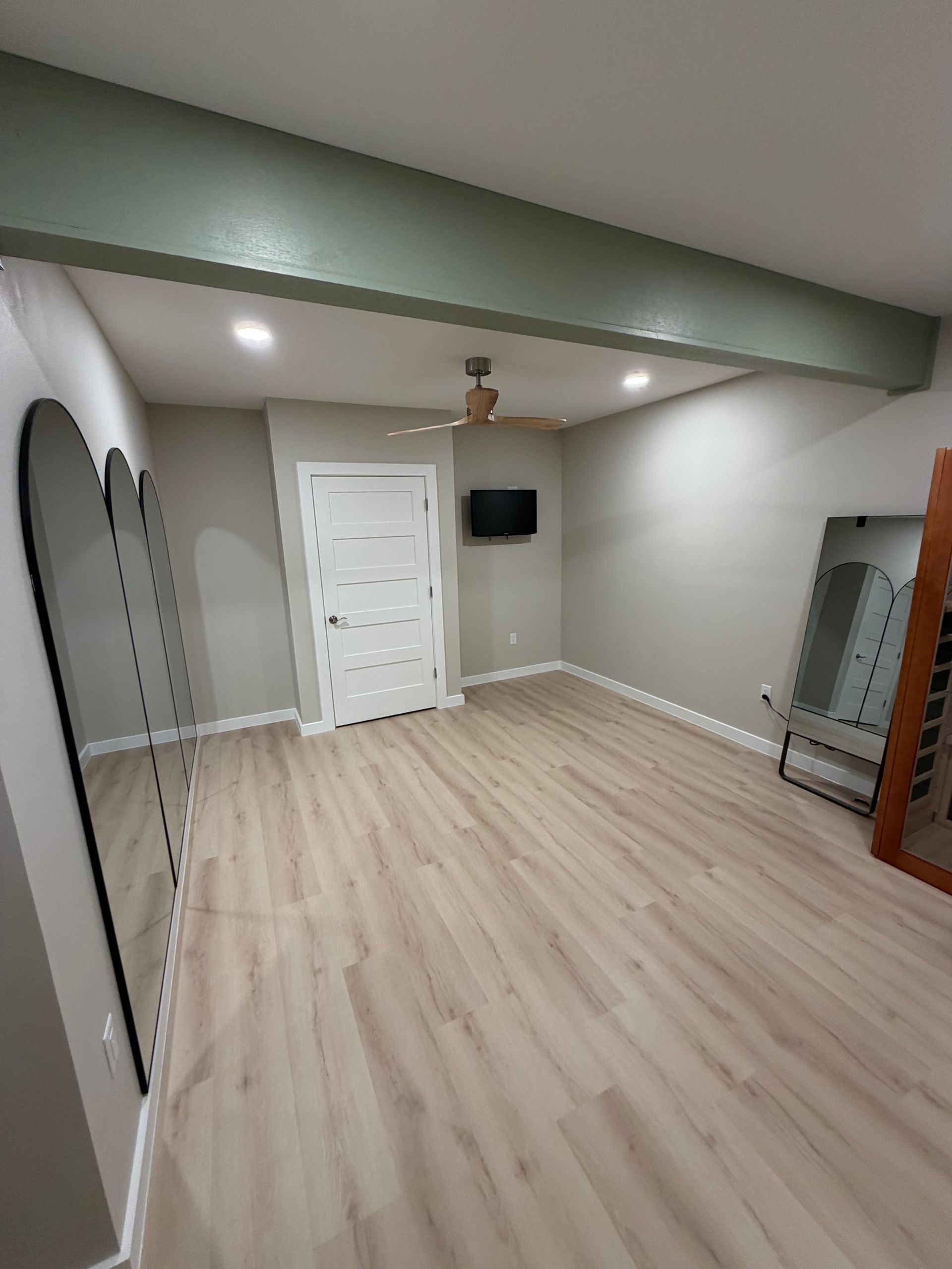 Empty room with light wood floors, mirrors, and a green beam on the ceiling.