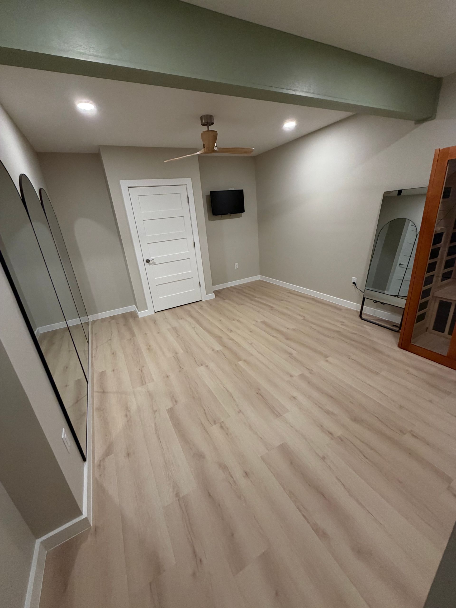 Empty room with wood-look flooring, white door, and a television. A ceiling fan and two full-length mirrors are present.