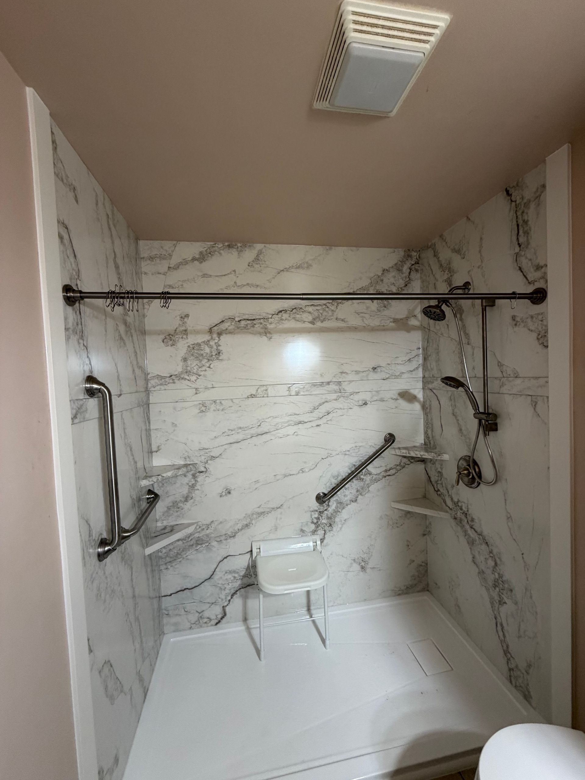 Accessible marble-tiled shower with grab bars, shower head, and fold-down seat.