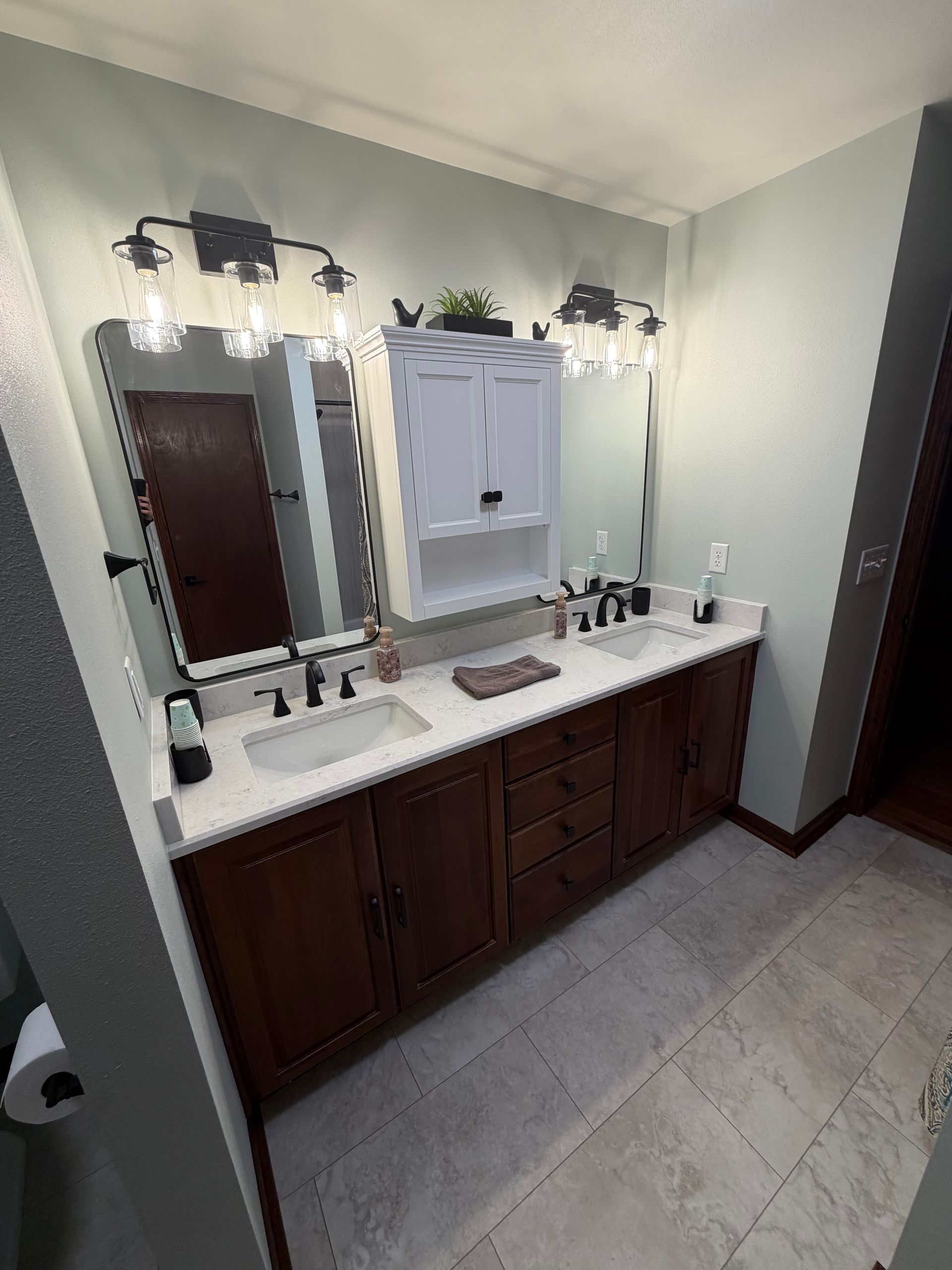 Bathroom with double vanity, brown cabinets, light-colored countertop, and gray tiled floor.