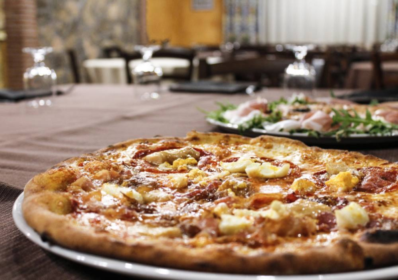Pizza sul tavolo di un ristorante, con un piatto di insalata sullo sfondo.