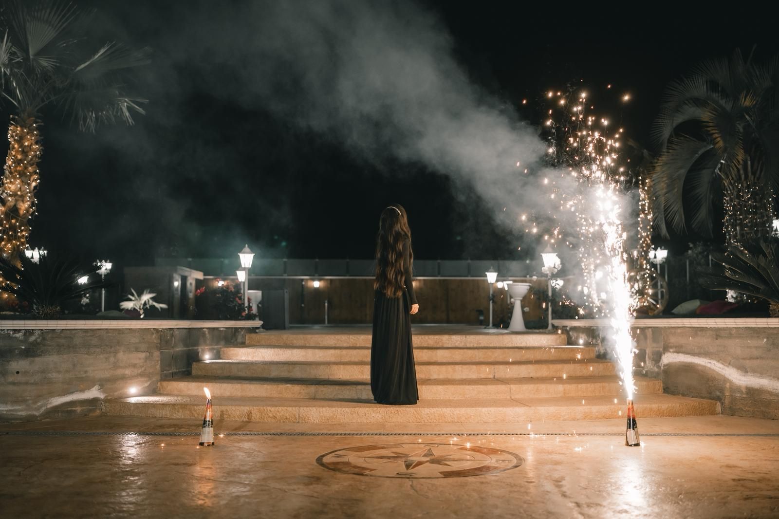 Una donna in abito nero sta in piedi davanti allo spettacolo pirotecnico notturno.