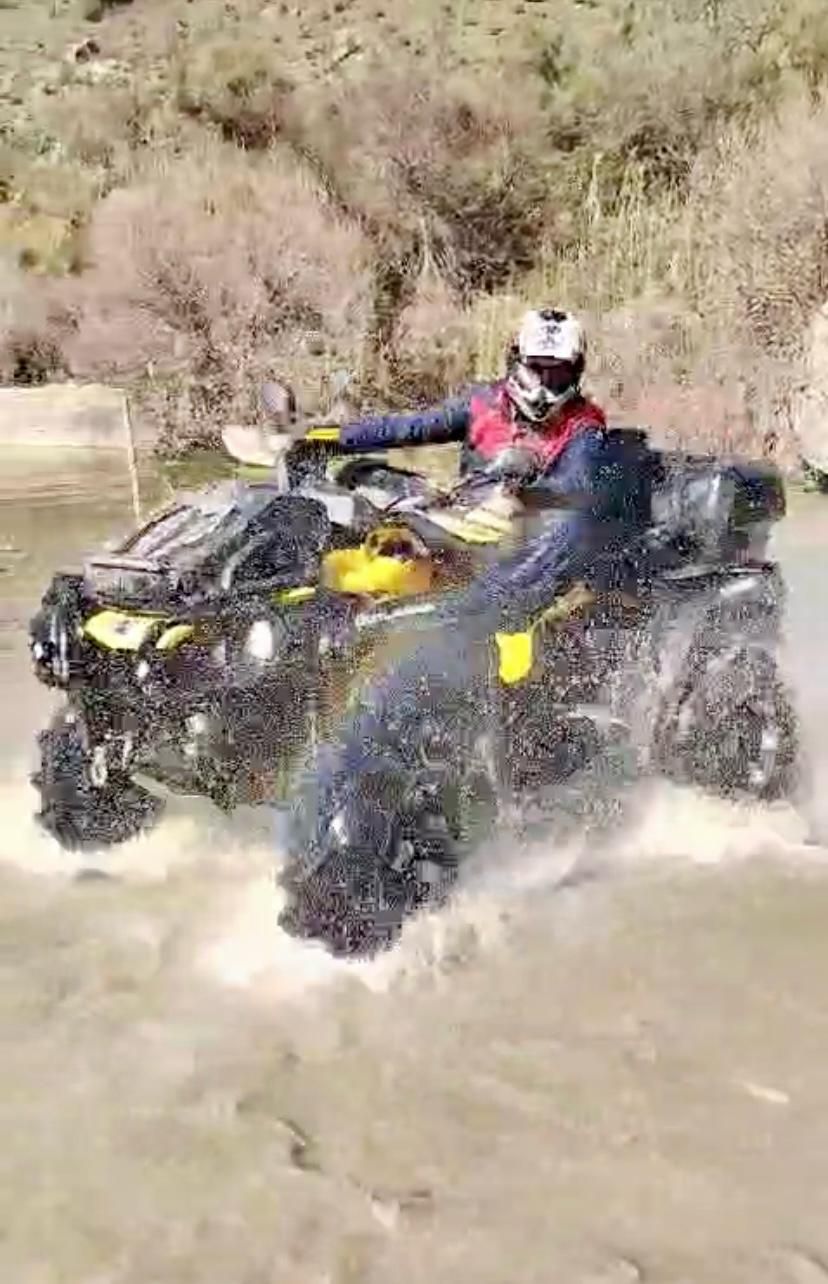 Persona su un quad che sguazza nell'acqua in un ambiente naturale e accidentato.