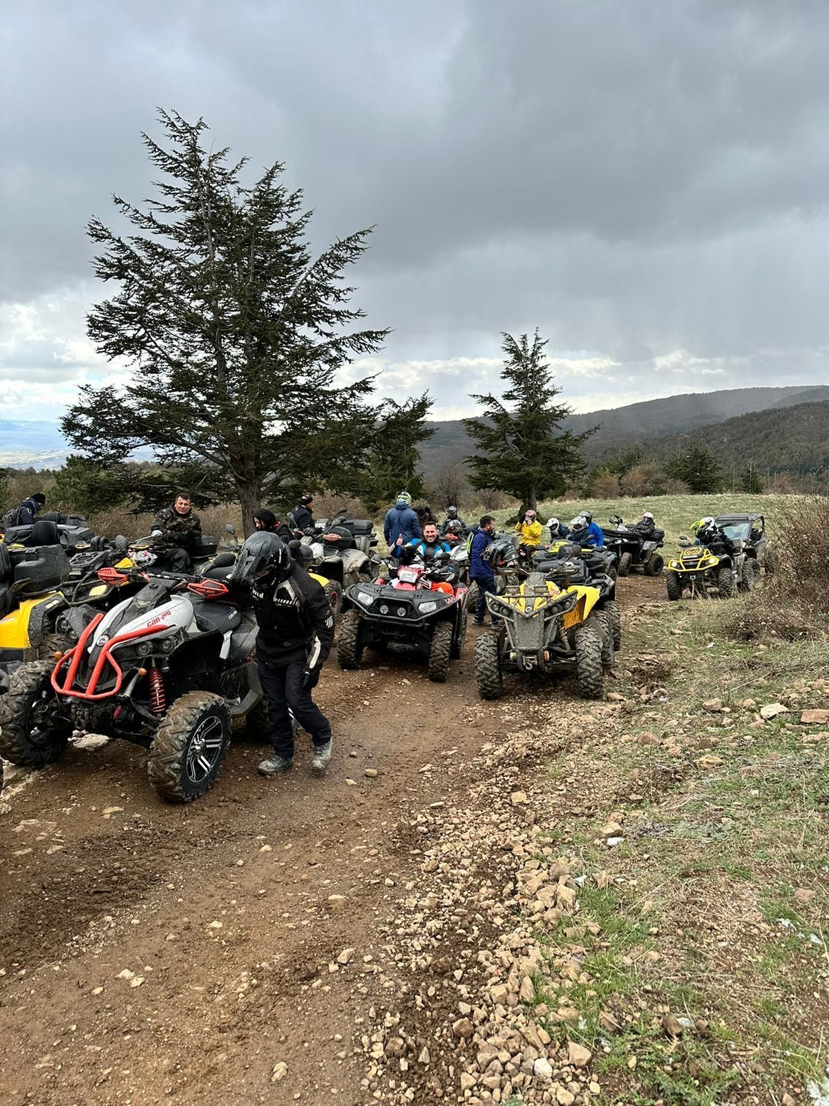 Un gruppo di persone su quad si è radunato su un sentiero sterrato in un paesaggio collinare e nuvoloso.