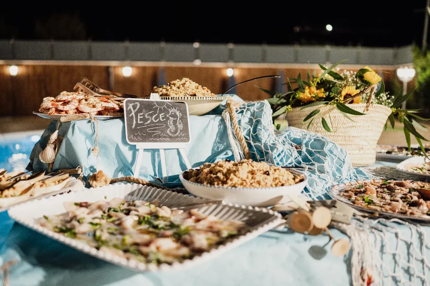 Un tavolo da buffet con vari piatti di pesce e decorazioni, allestito all'aperto vicino a una piscina.