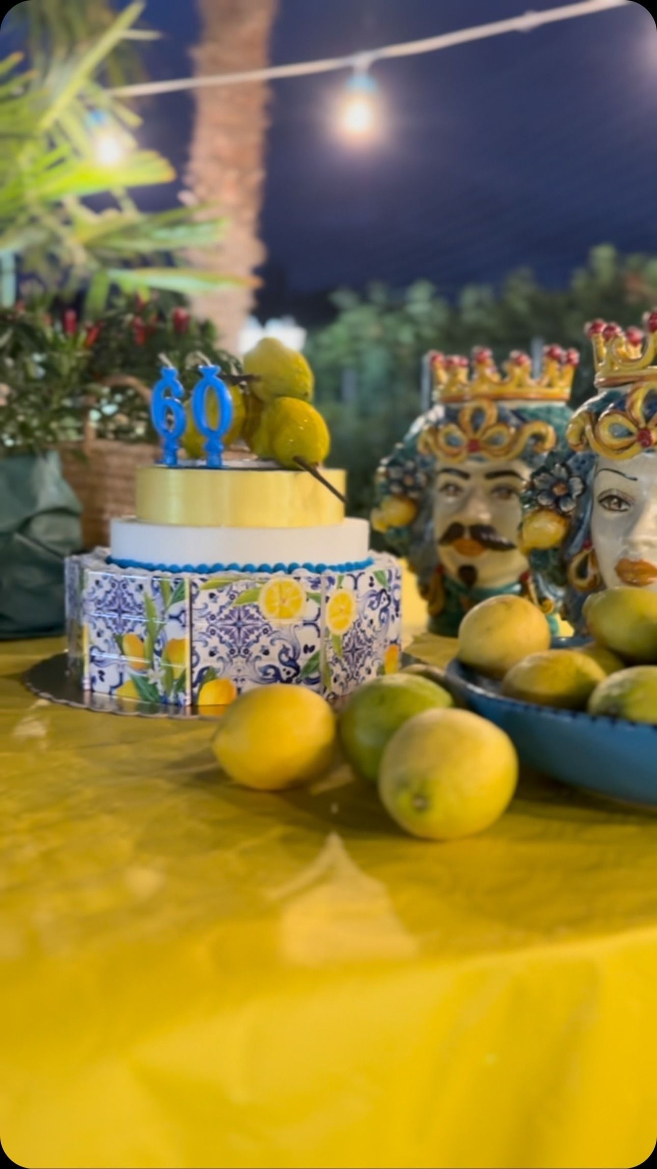 Torta con limoni e teste di ceramica su un tavolo con tovaglia gialla di notte.