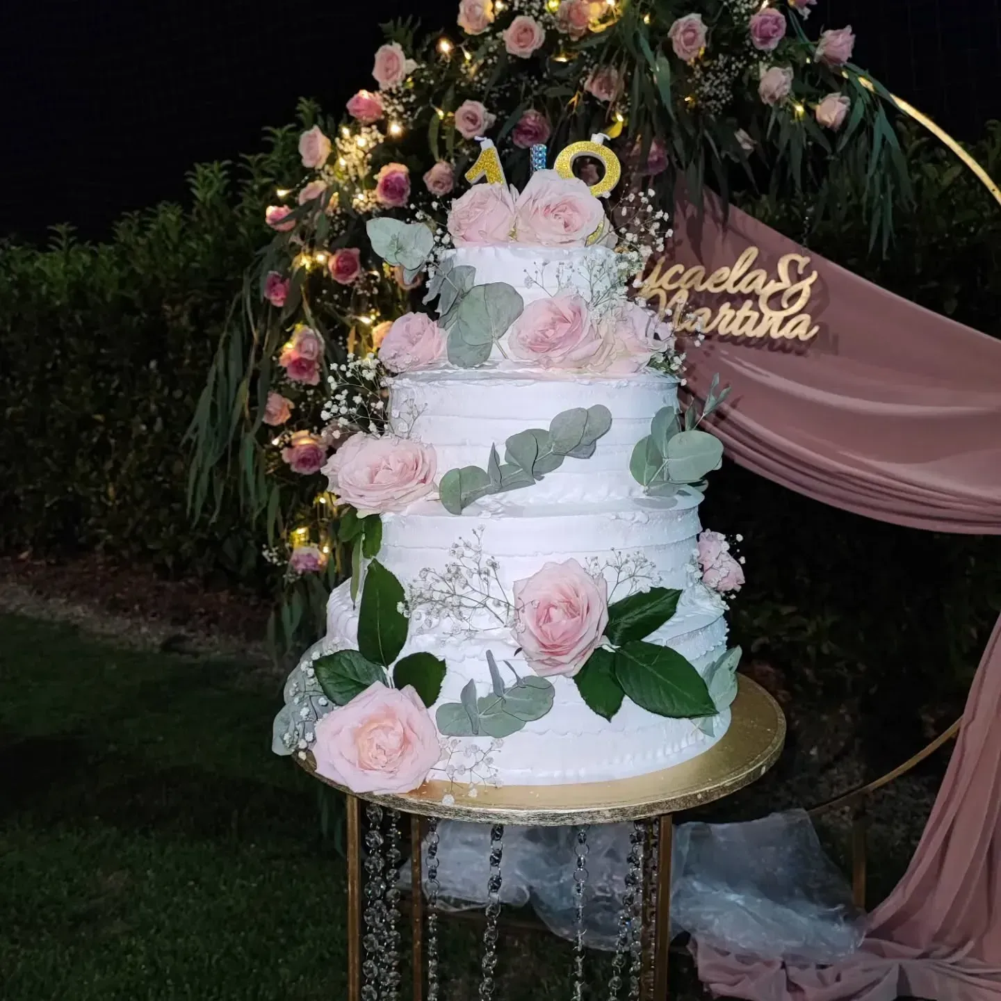 Torta nuziale con rose rosa e verde. Arco floreale e supporto dorato.