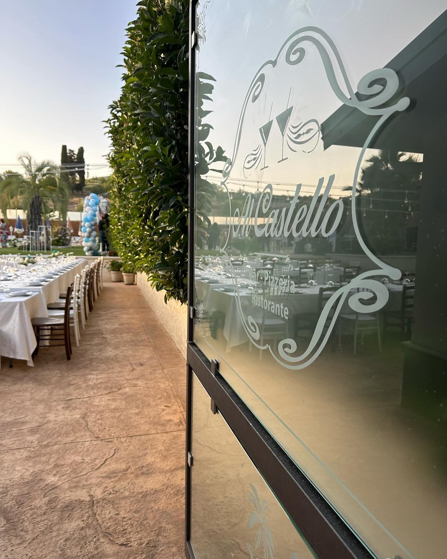 Porta in vetro con logo che raffigura una zona pranzo all'aperto apparecchiata per un pasto.