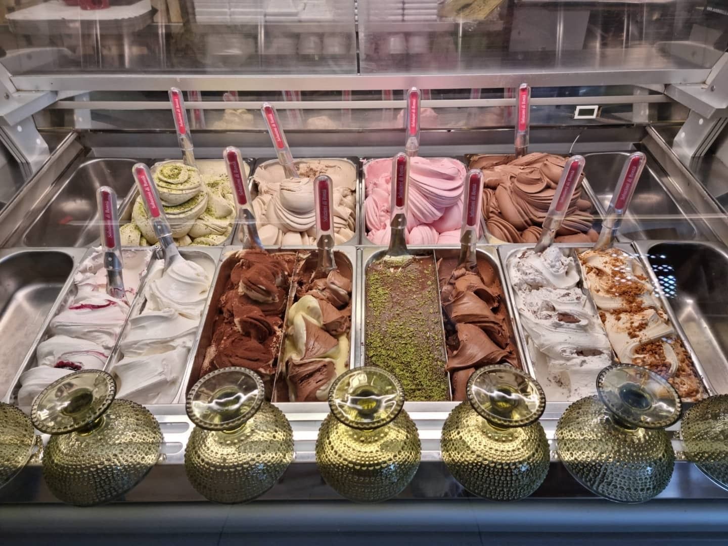 Vetrina per gelato con vari gusti, vaschette argentate, palline e decorazioni dorate.