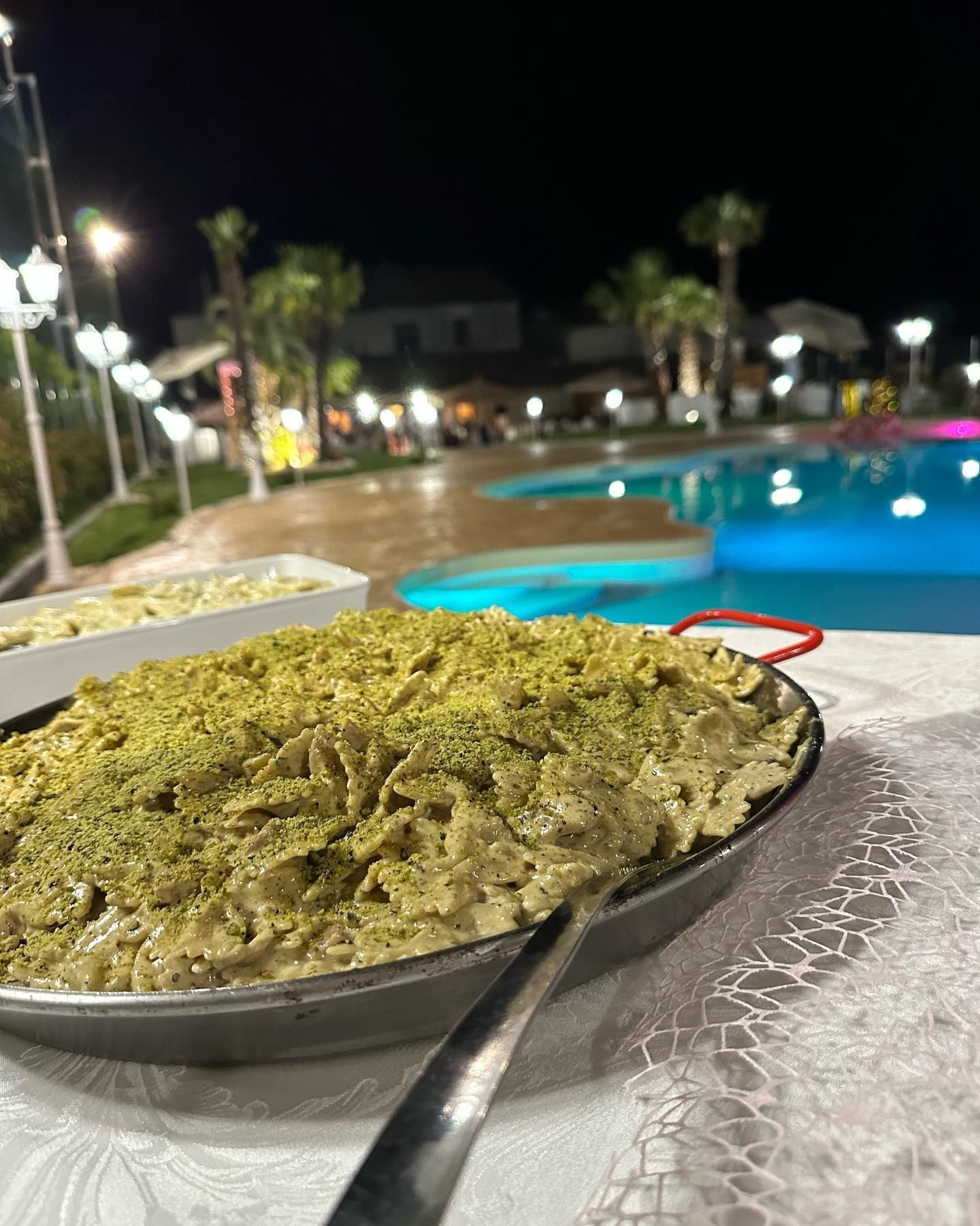 Piatto di pasta con salsa verde e pistacchi, vicino a una piscina di notte.