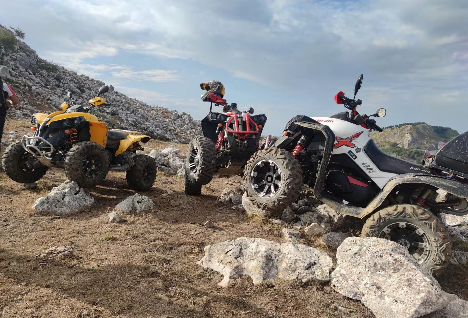 Tre quad su un paesaggio roccioso e marrone: uno giallo, uno rosso e nero e uno bianco e rosso.