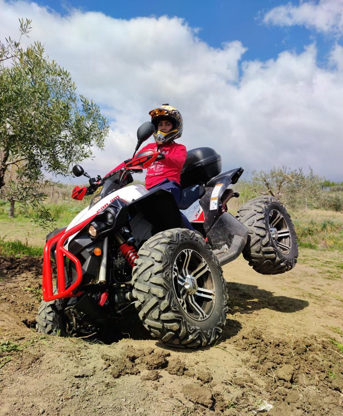 Persona su un quad, con le ruote anteriori in un fosso di terra e la ruota posteriore sollevata. Soleggiato, all'aperto.